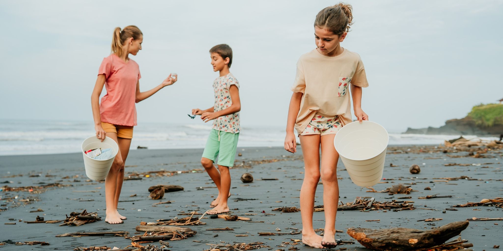 Three kids in organic clothes picking up trash on the beach